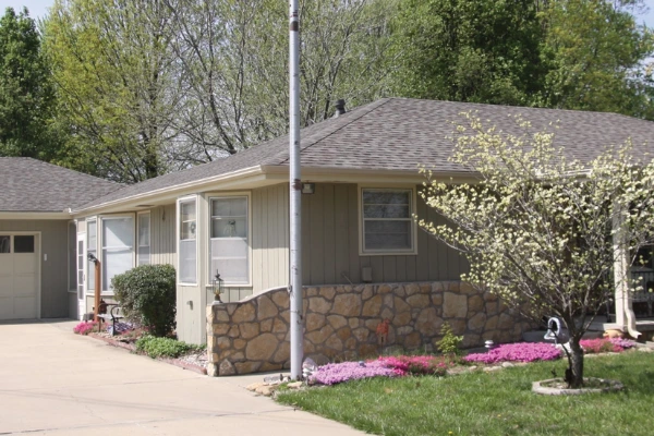 A completed residential roofing project featuring clean, grey asphalt shingles on a ranch-style home with tan siding and stone accents.